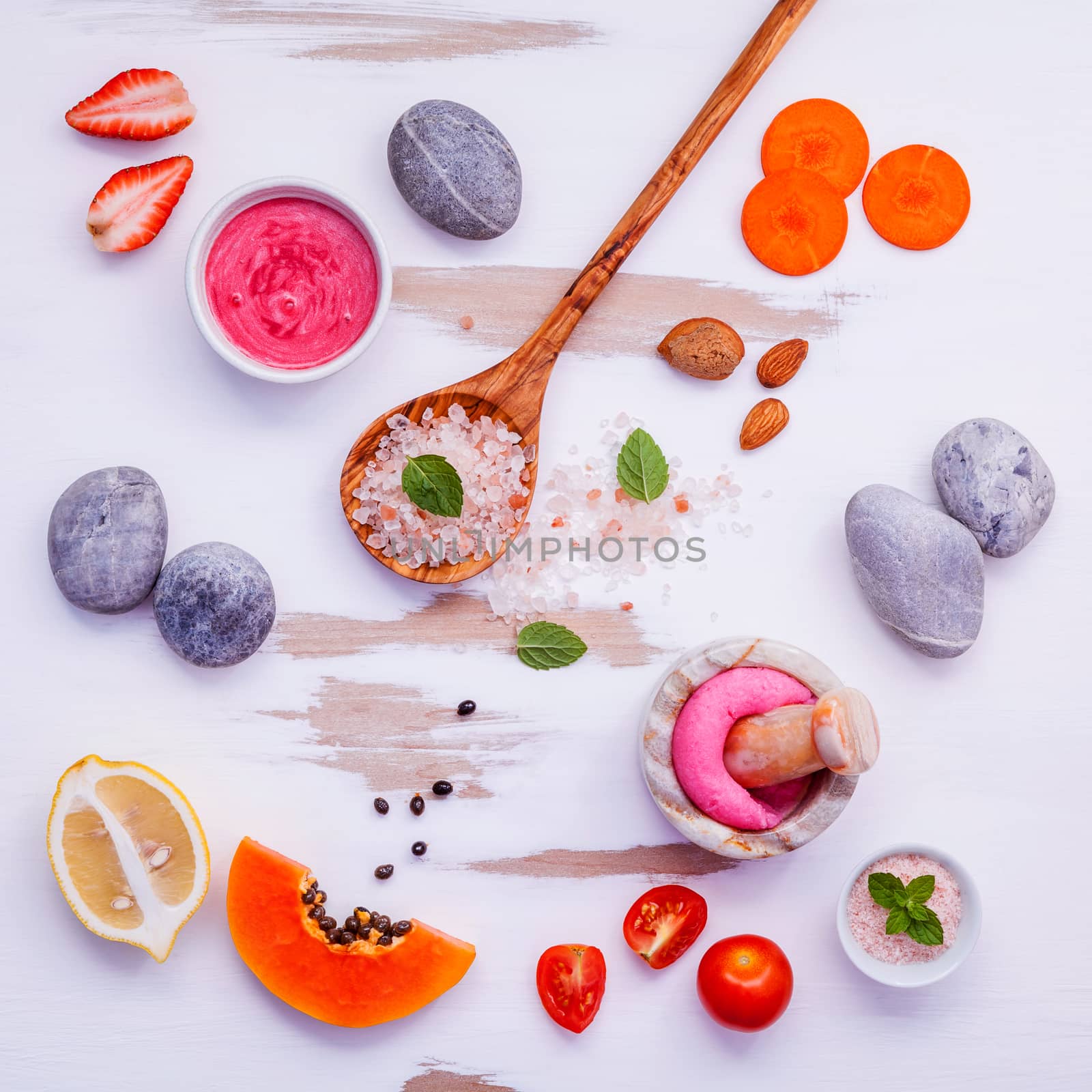 Homemade skin care and body scrubs with red natural ingredients strawberry , tomato ,himalayan salt, ripe papaya, carrot and spa stone setup on white wooden background with flat lay. Zen spa and oriental spa theme.