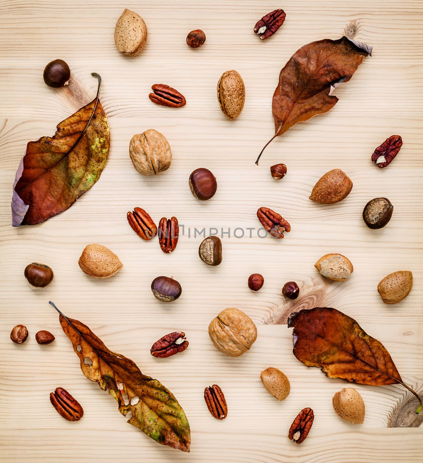 Different kinds of nuts walnuts kernels ,hazelnuts, almond kernels and pecan with dried orange leaves set up on rustic wooden background.