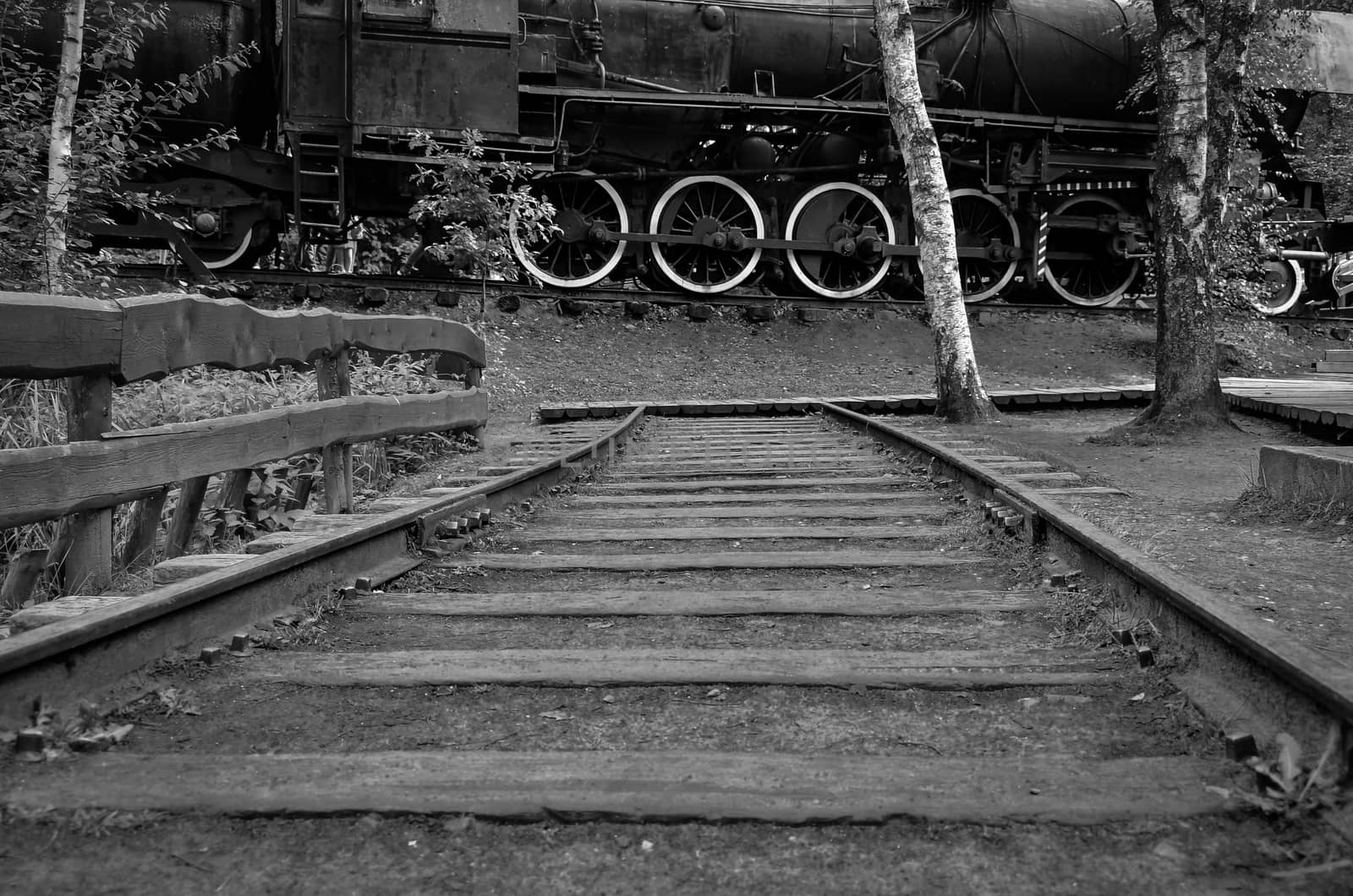 End of Train tracks against old steam locomotive in black and white photo
