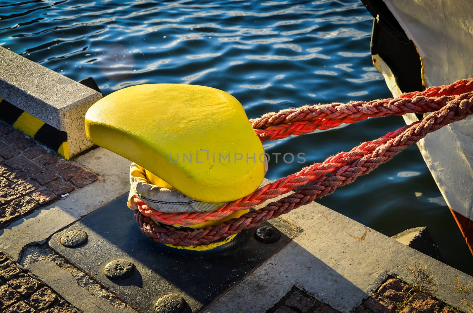 Rope tied in a knot on a bollard. Mooring rope wrapped around the cleat on sea background. Metal capstan in harbor for the mooring of yachts and boats