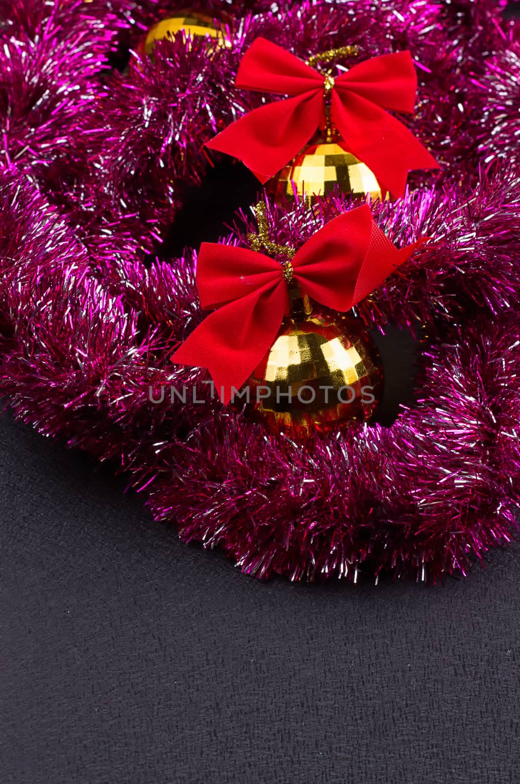 Beautiful Christmas decoration. Gold Christmas balls and bright sparkling golden tinsel with red bows on black background