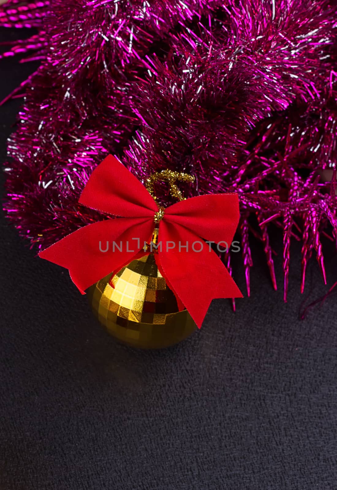 Beautiful Christmas decoration. Gold Christmas balls and bright sparkling golden tinsel with red bows on black background