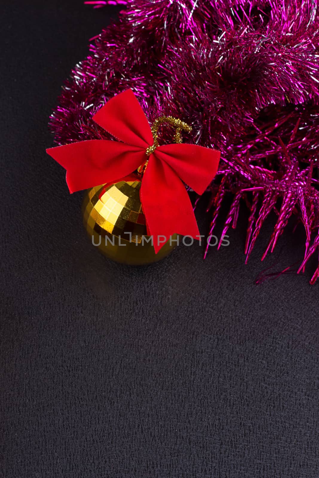 Beautiful Christmas decoration. Gold Christmas balls and bright sparkling golden tinsel with red bows on black background
