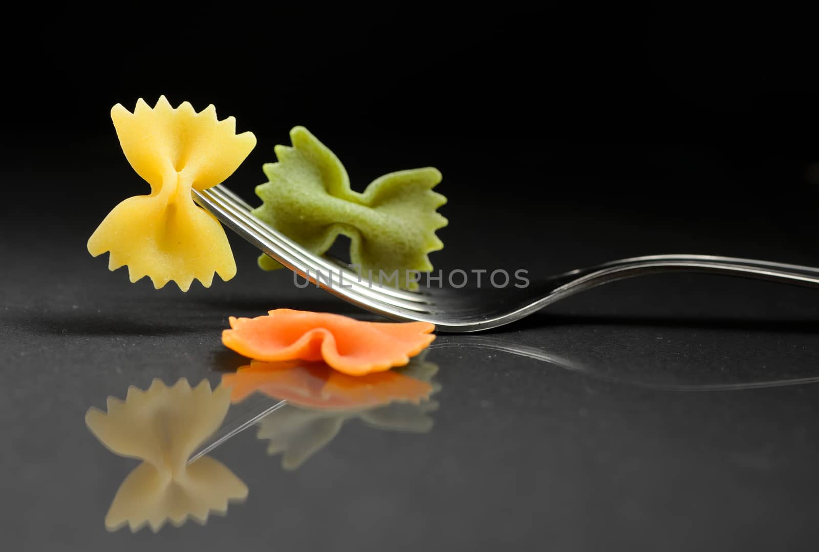 pasta farfalle on a fork on black background