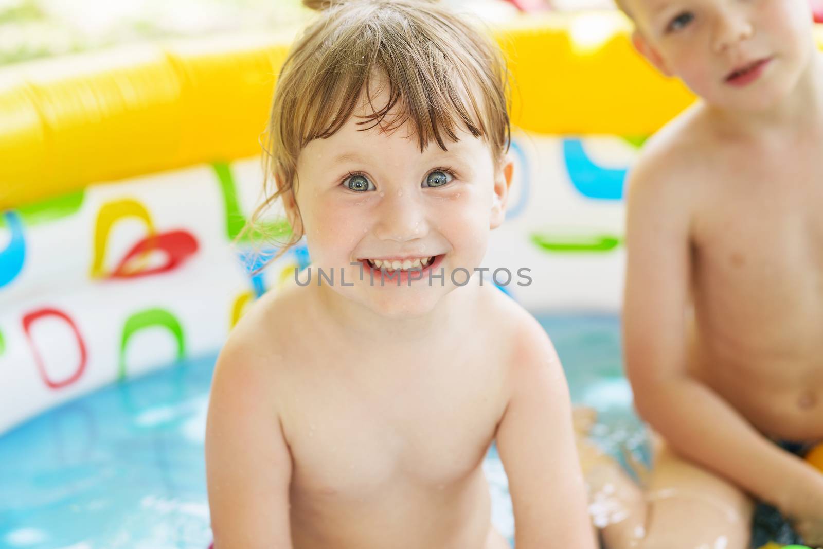 Little children bathe in yellow Inflatable Swimming Paddling Pool outdoors in hot summer day. Kids in Swim Pool