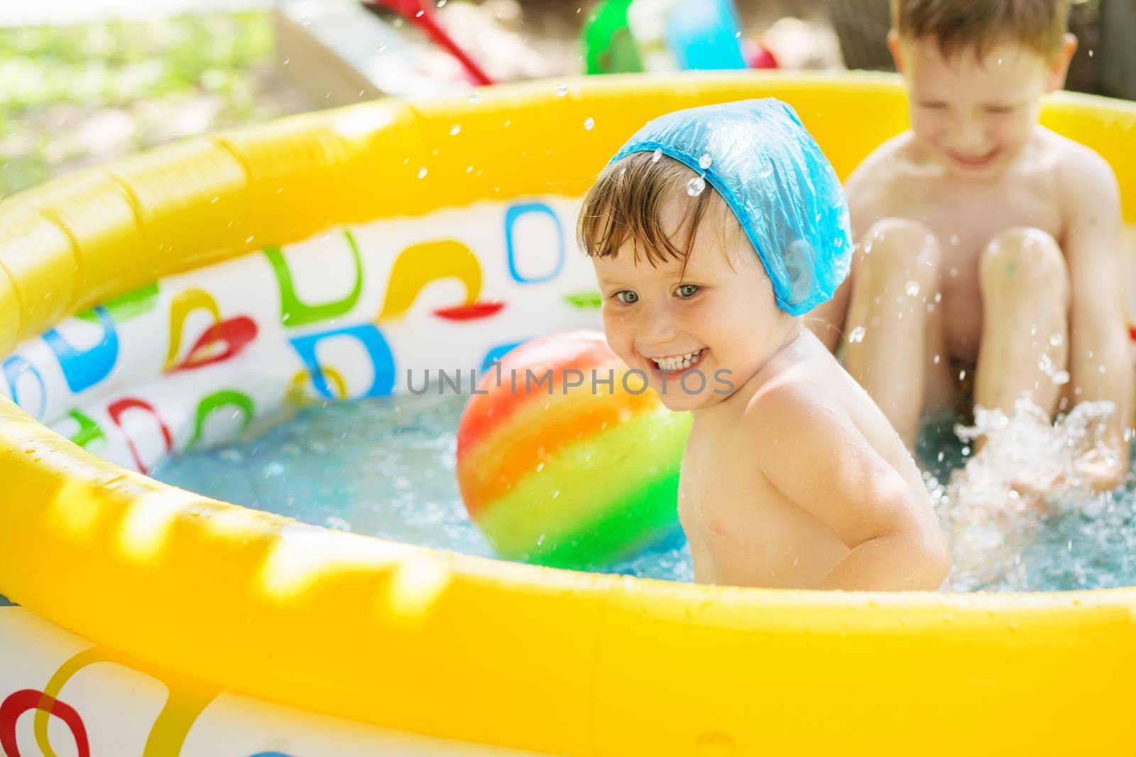 Little children bathe in yellow Inflatable Swimming Paddling Pool outdoors in hot summer day. Kids splashing water and having fun in Swim Pool
