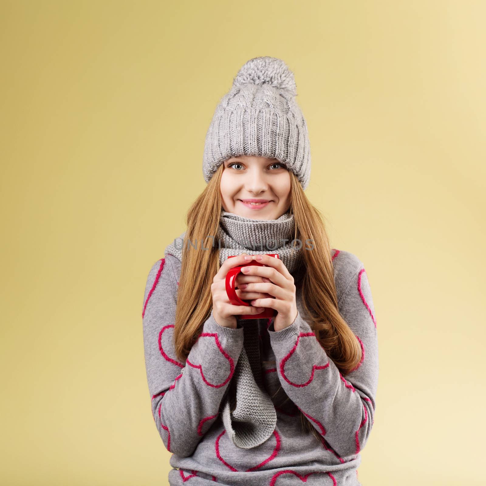 girl wearing gray woolen cap and scarf holding a red cup against by natazhekova