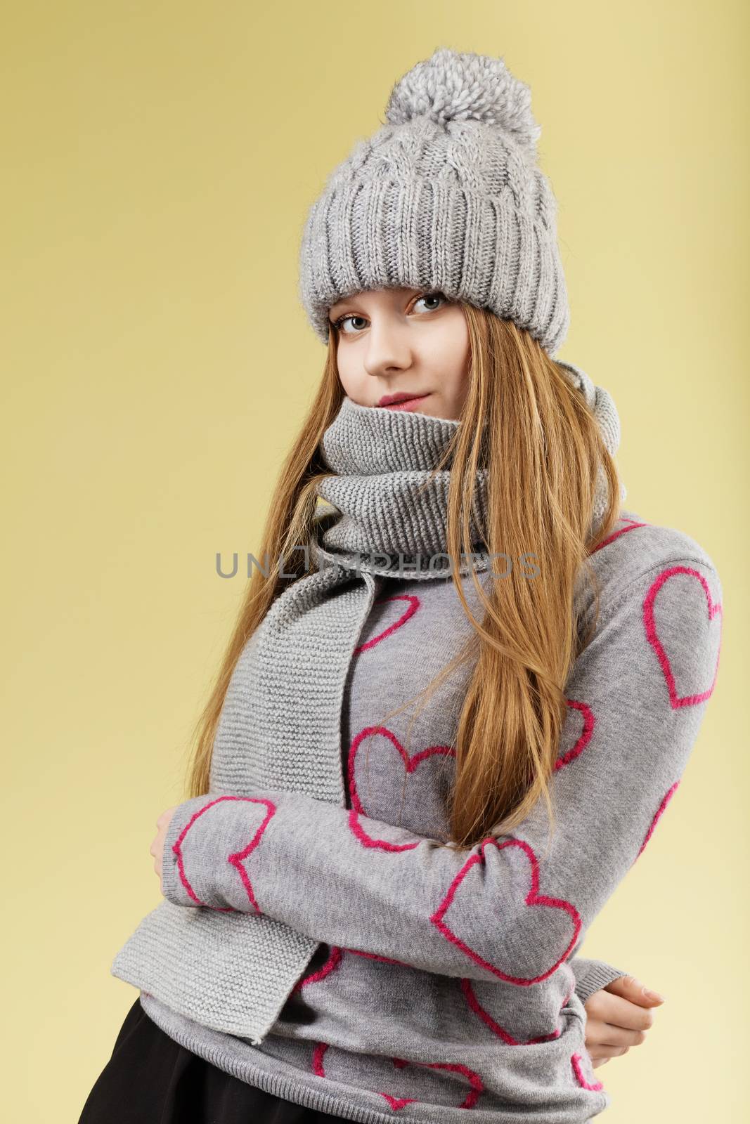 Cute teenage girl wearing gray woolen cap and scarf against yellow background