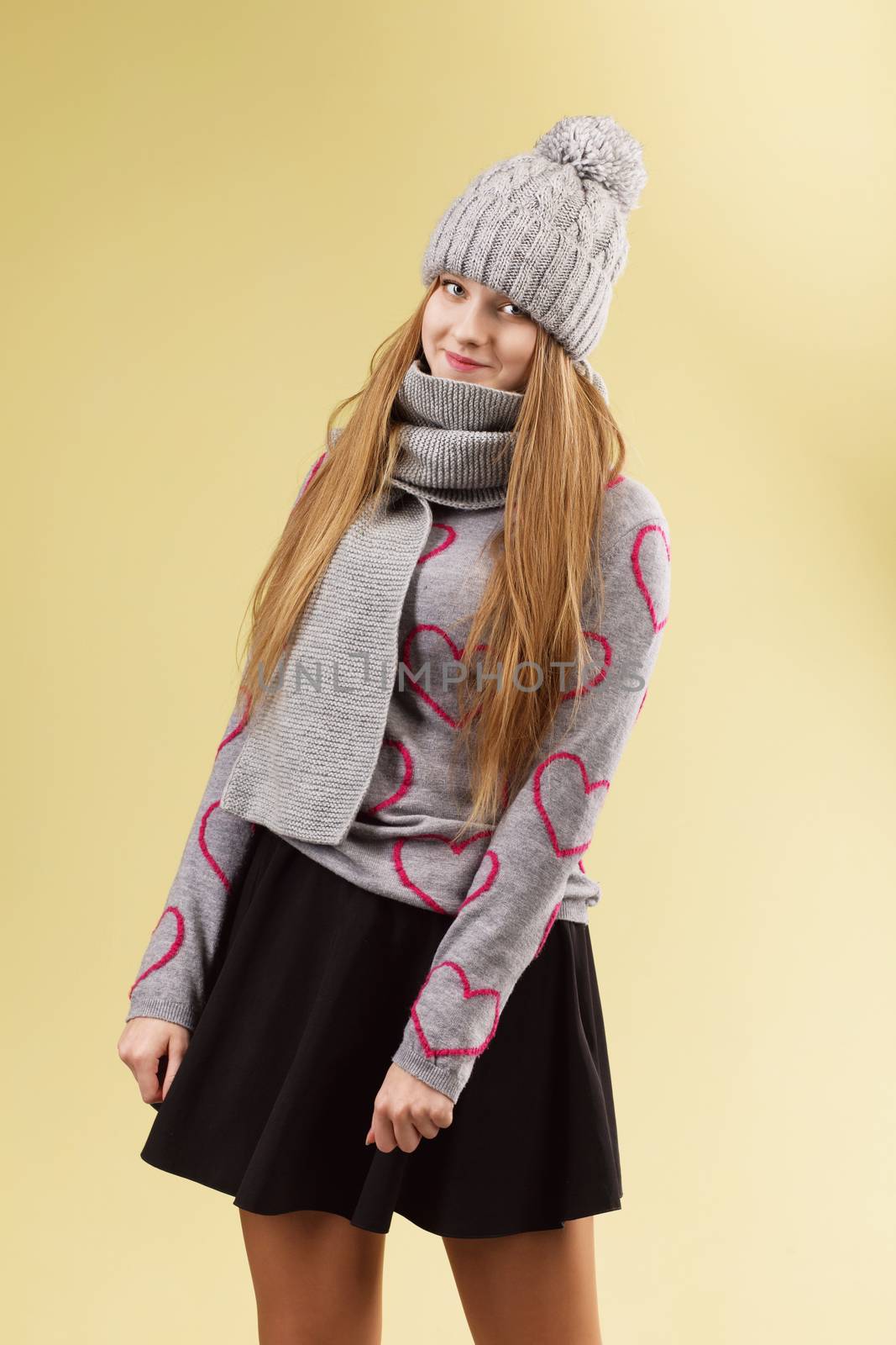 Cute teenage girl wearing gray woolen cap and scarf against yellow background