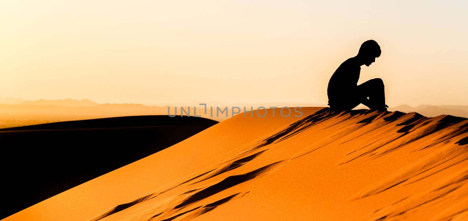 Panoramic view of silhouette of meditating young man sitting on top of a dune of sahara