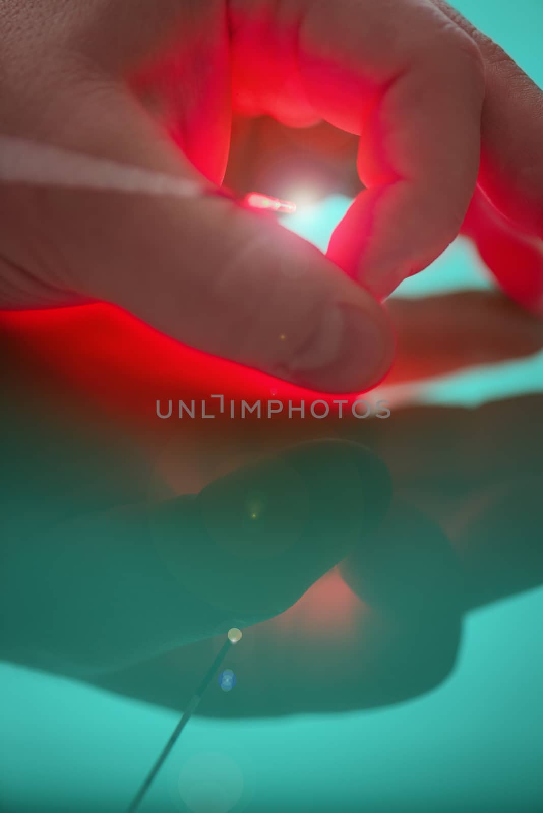 Source of bright light on the end of the probe for treatment by means of the laser between big and forefingers of the left hand of the person with reflection.