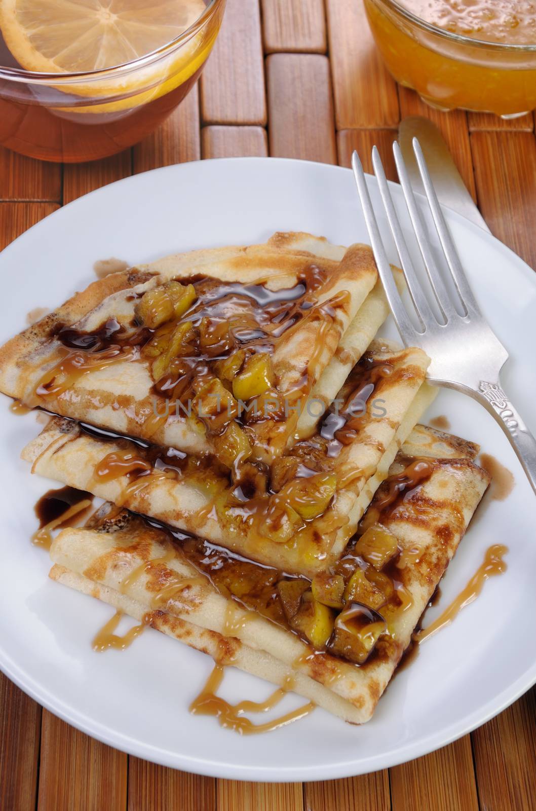 Breakfast pancakes on apples with caramel and chocolate and cup of tea