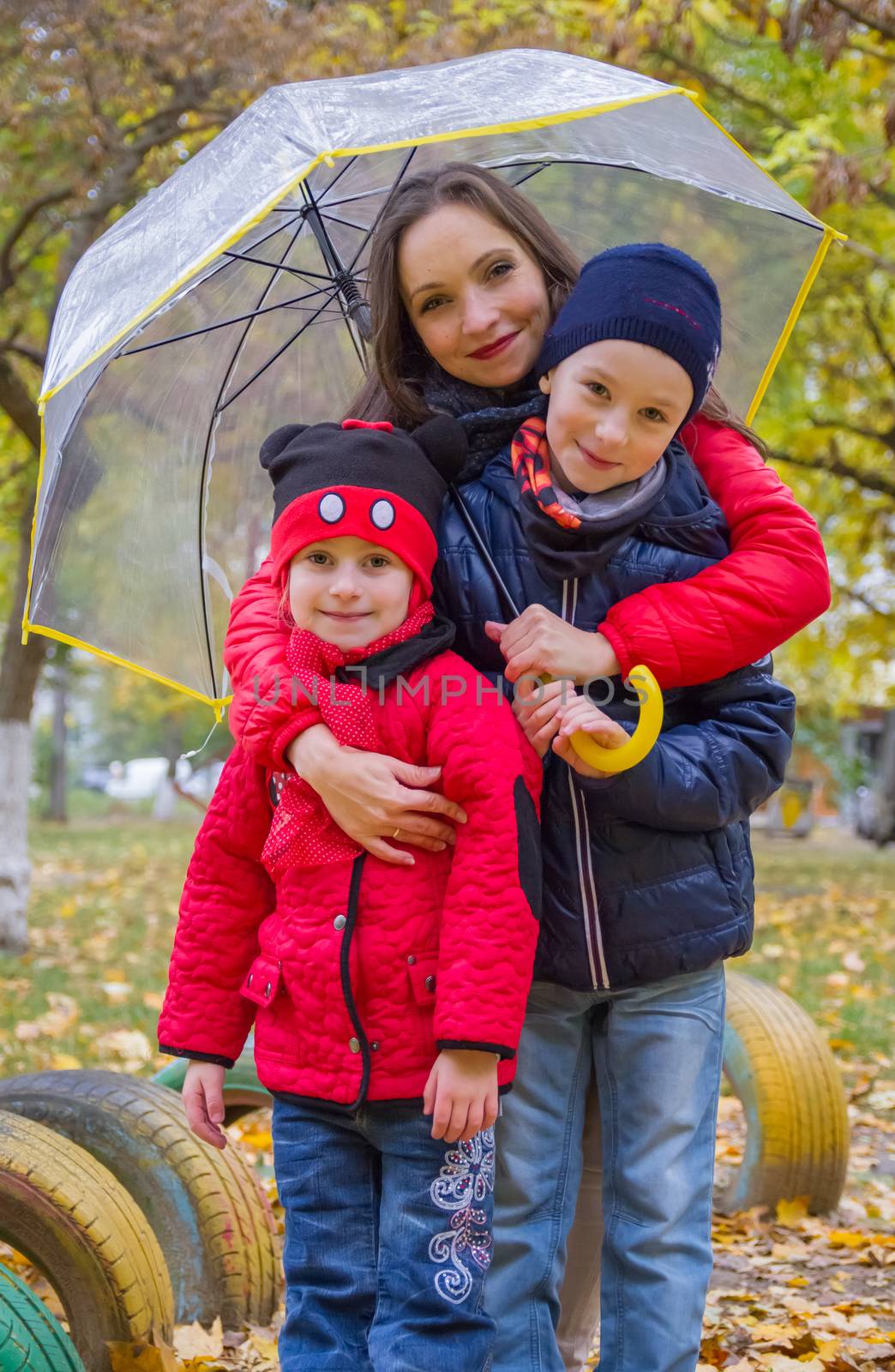 Mother with two kids under umbrella in autumn