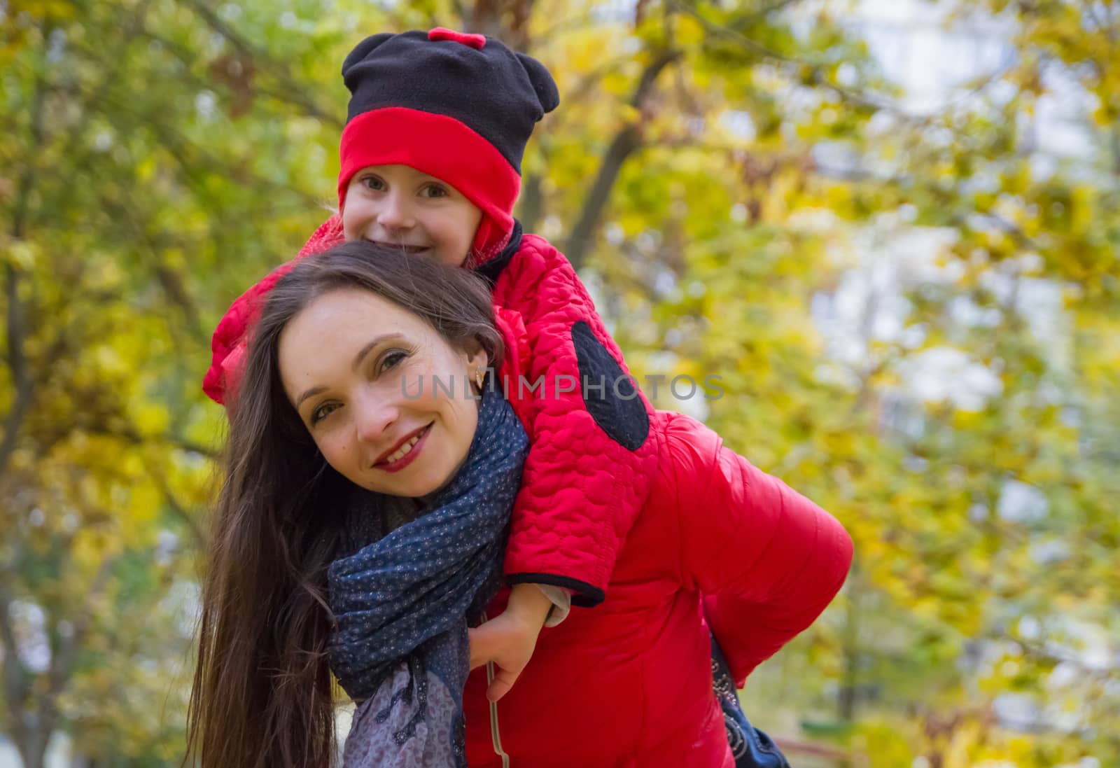 Mother giving daughter piggyback ride in autumn park