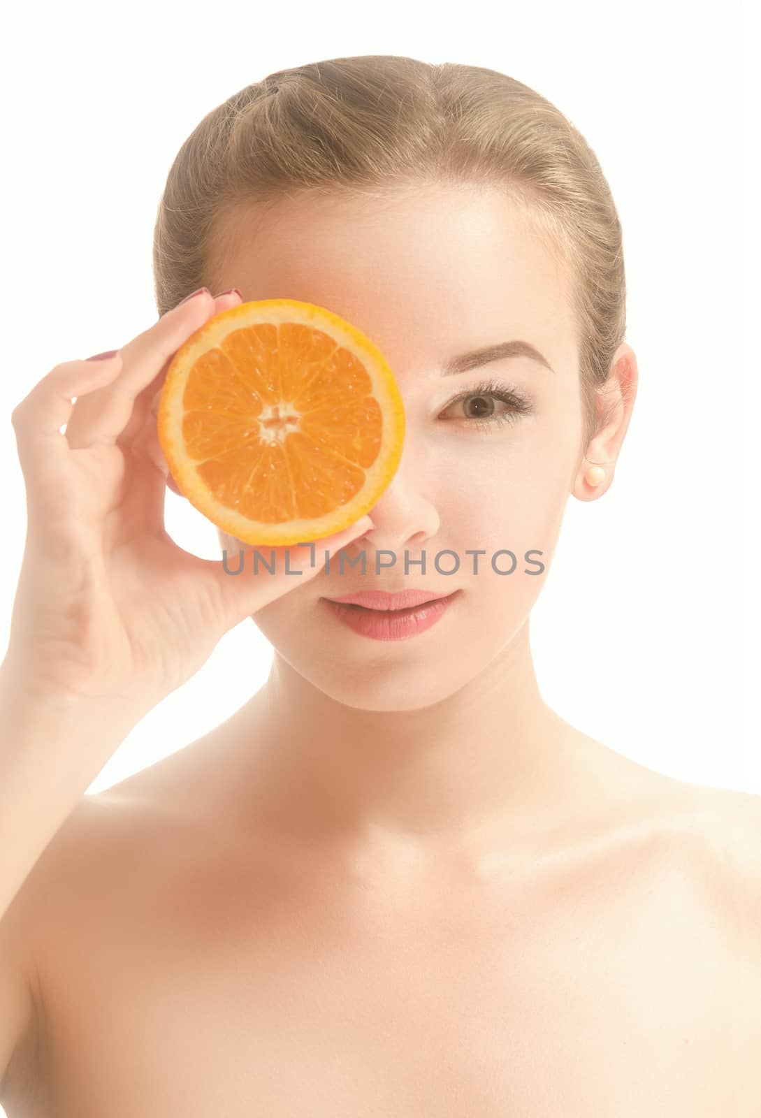 Attractive young woman with a slice of orange in front of her eyes, which stands on white background and smiling