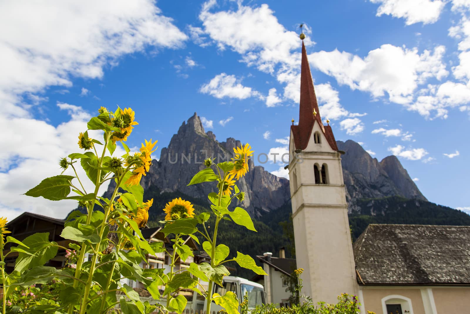 Seiser Alm Schlern, IT- September 19. Botton view of the St. Mary's Assumption with sunflowers in the foreground and Seiser Alm on the background