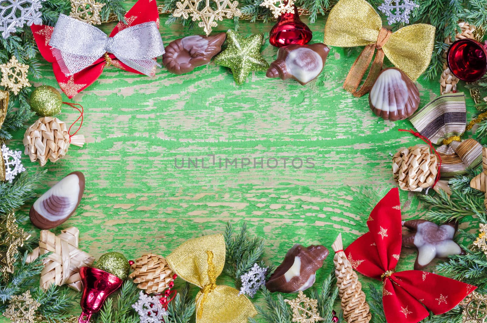 Vignette of Christmas ornaments,sprigs of juniper and chocolate. Old wooden background,painted green, lots of space for inscriptions.
