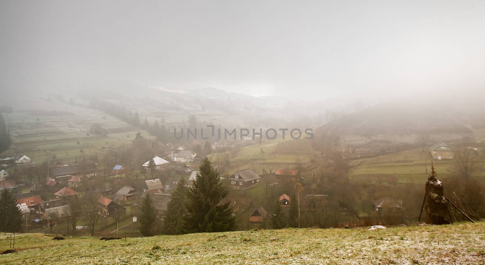 Late autumn misty morning in a village. First Snow in mountains