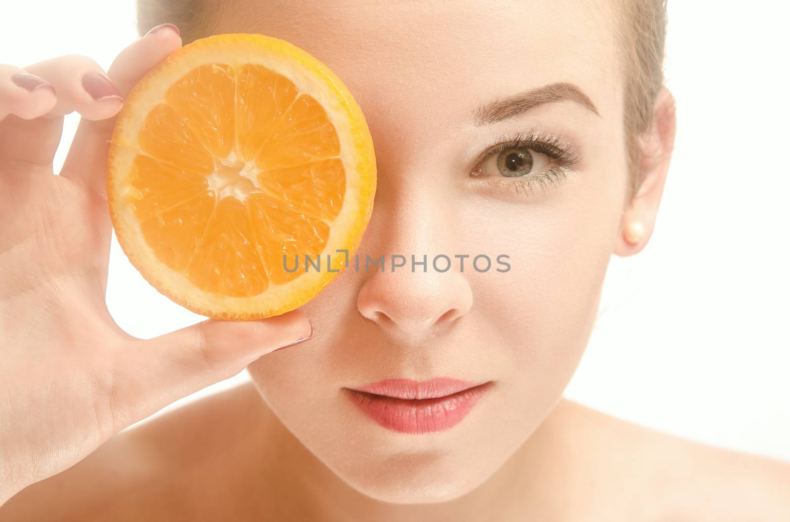 Beautiful young seminude woman of European appearance holds an orange in front of her eyes, standing on white background