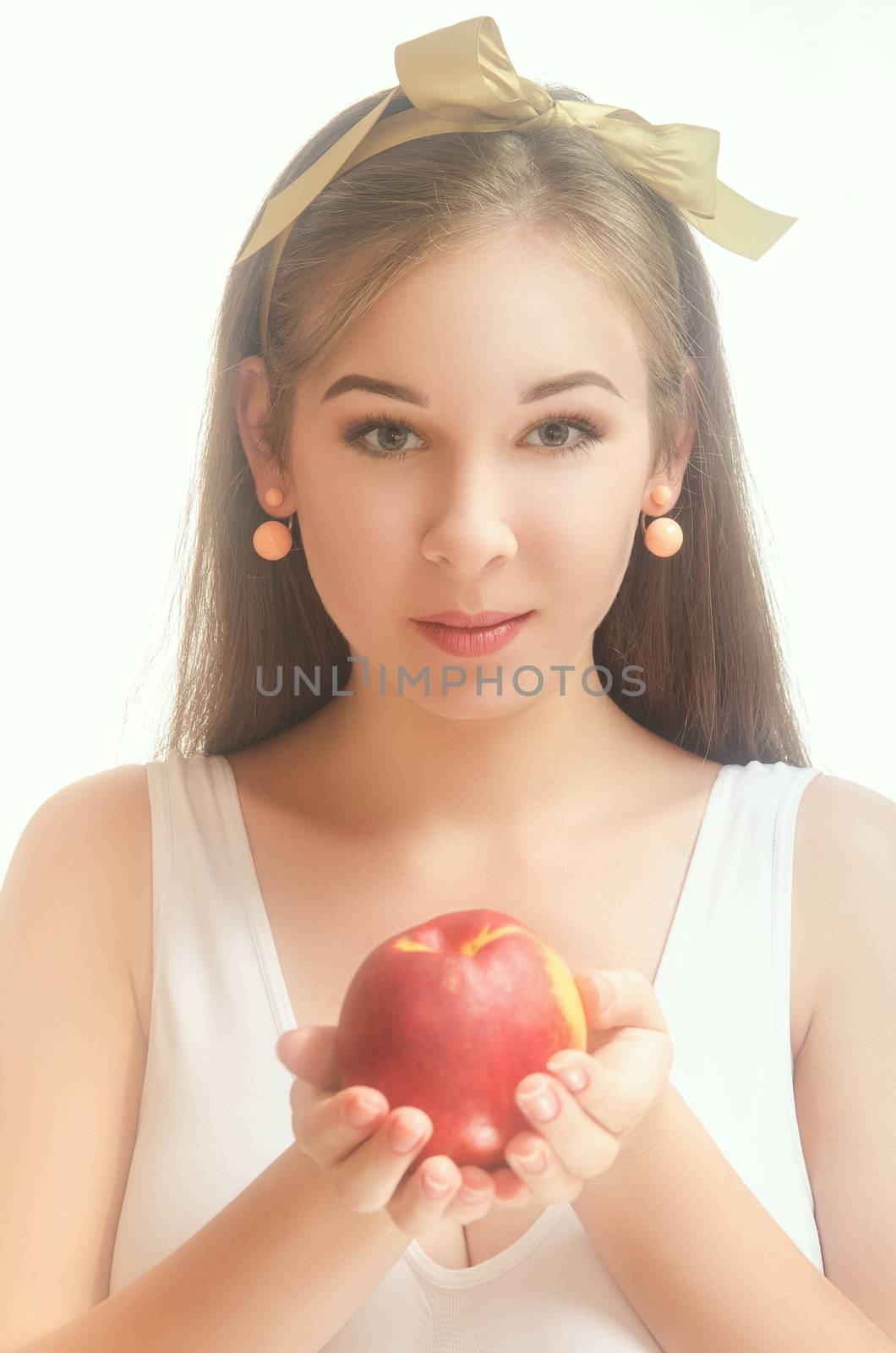 Young beautiful woman in a white T-shirt with a bow on her hair holding a peach in her hands. White background