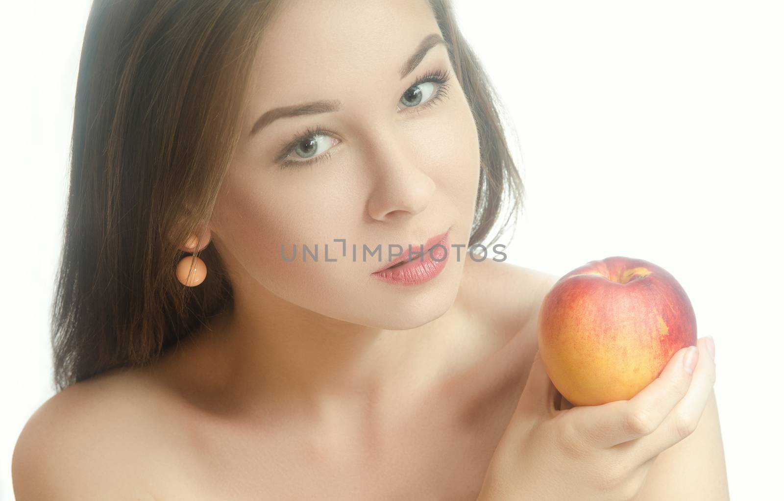Young tender girl with flowing hair holding a peach in the hand near the neck. White background