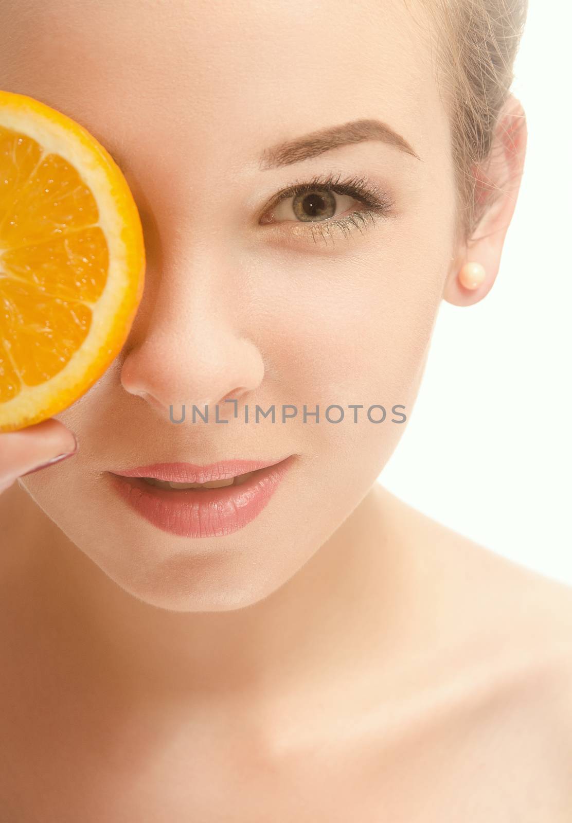 Face of a beautiful young woman who is holding a half of orange slices in front of his eyes and smiling. White background