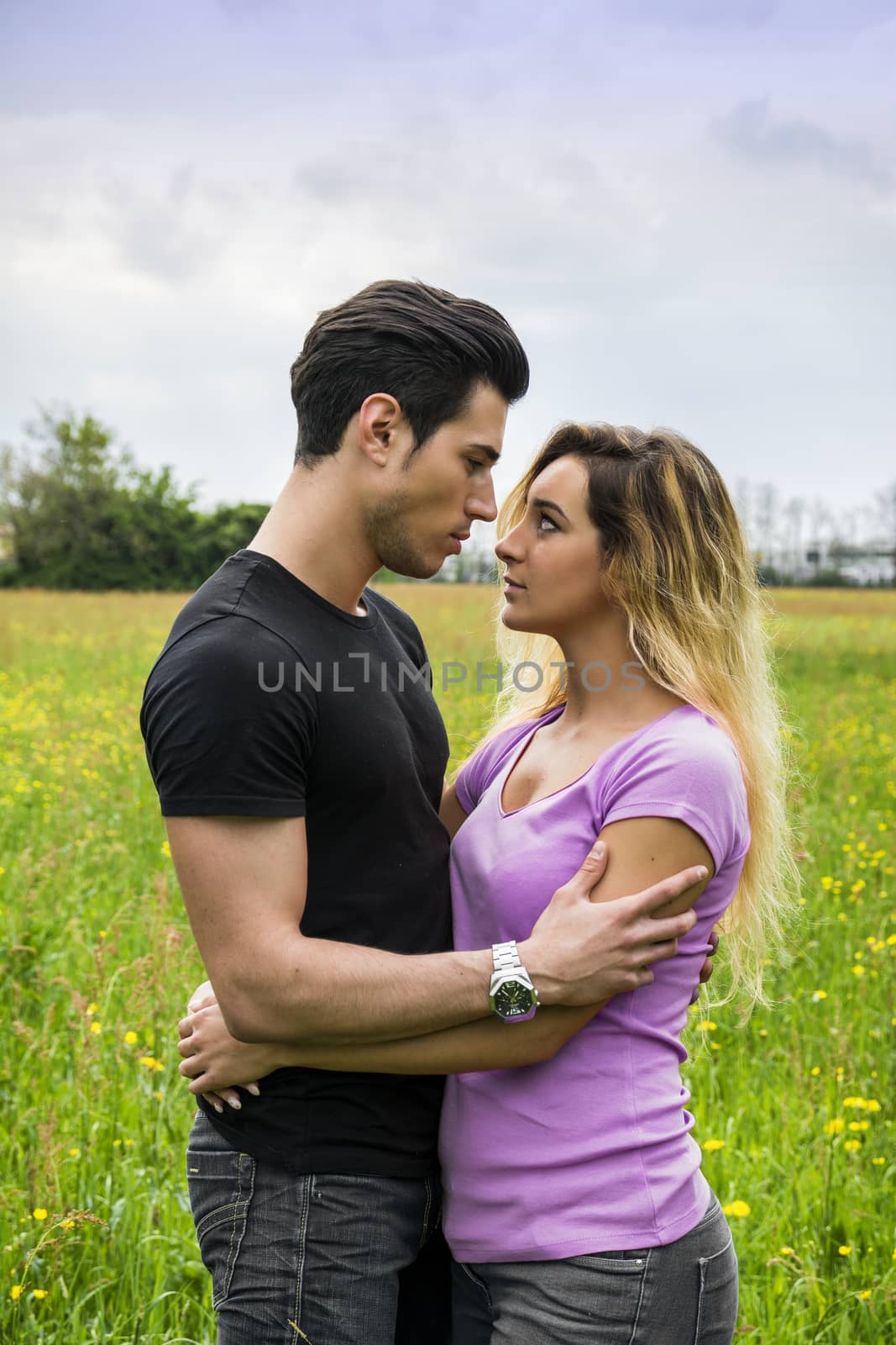 Boyfriend and girlfriend standing in countryside in green luscious field, embracing each other and cuddling, showing romantic love