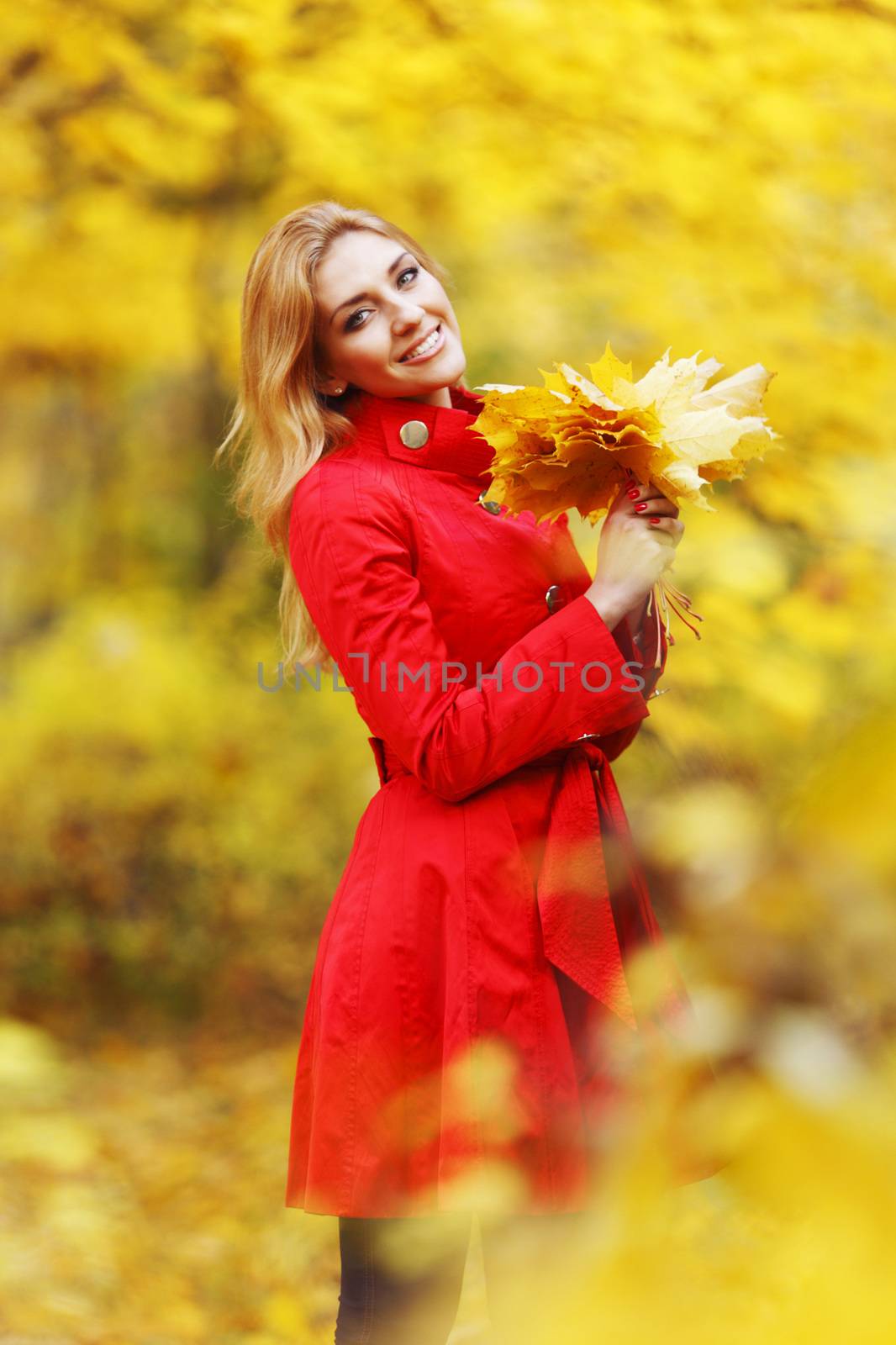 Young beautiful woman posing in autumn park with a bunch of dry leaves
