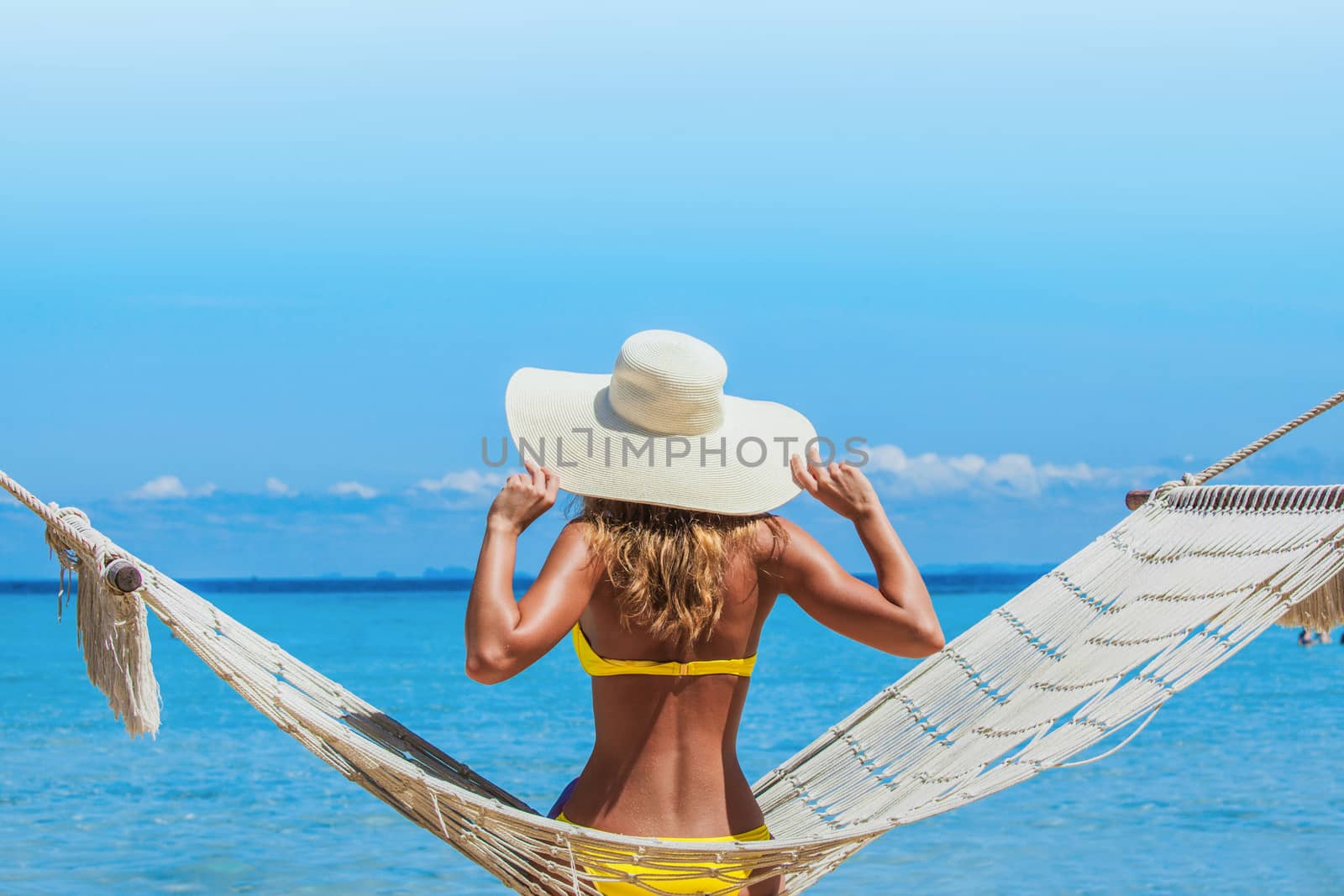 Woman in sunhat swinging in hummock on blue sea background