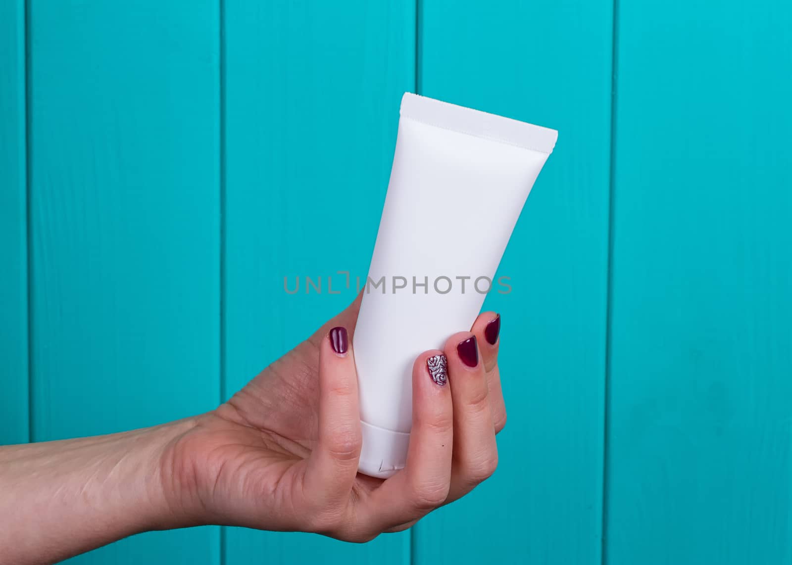 Woman's beautiful hands with care cream tube on the blue background