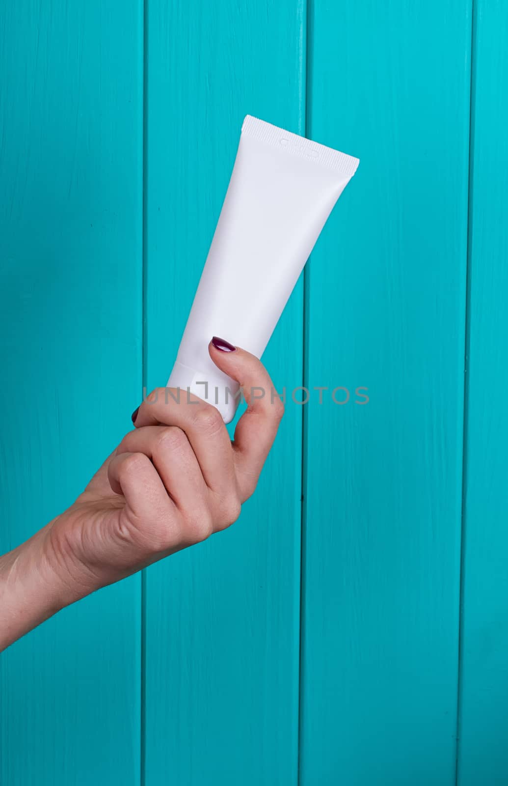 Woman's beautiful hands with care cream tube on the blue background