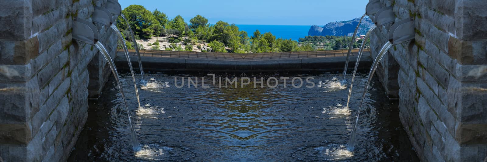 Modern fountain with six spotlighted water in the background sea and countryside.