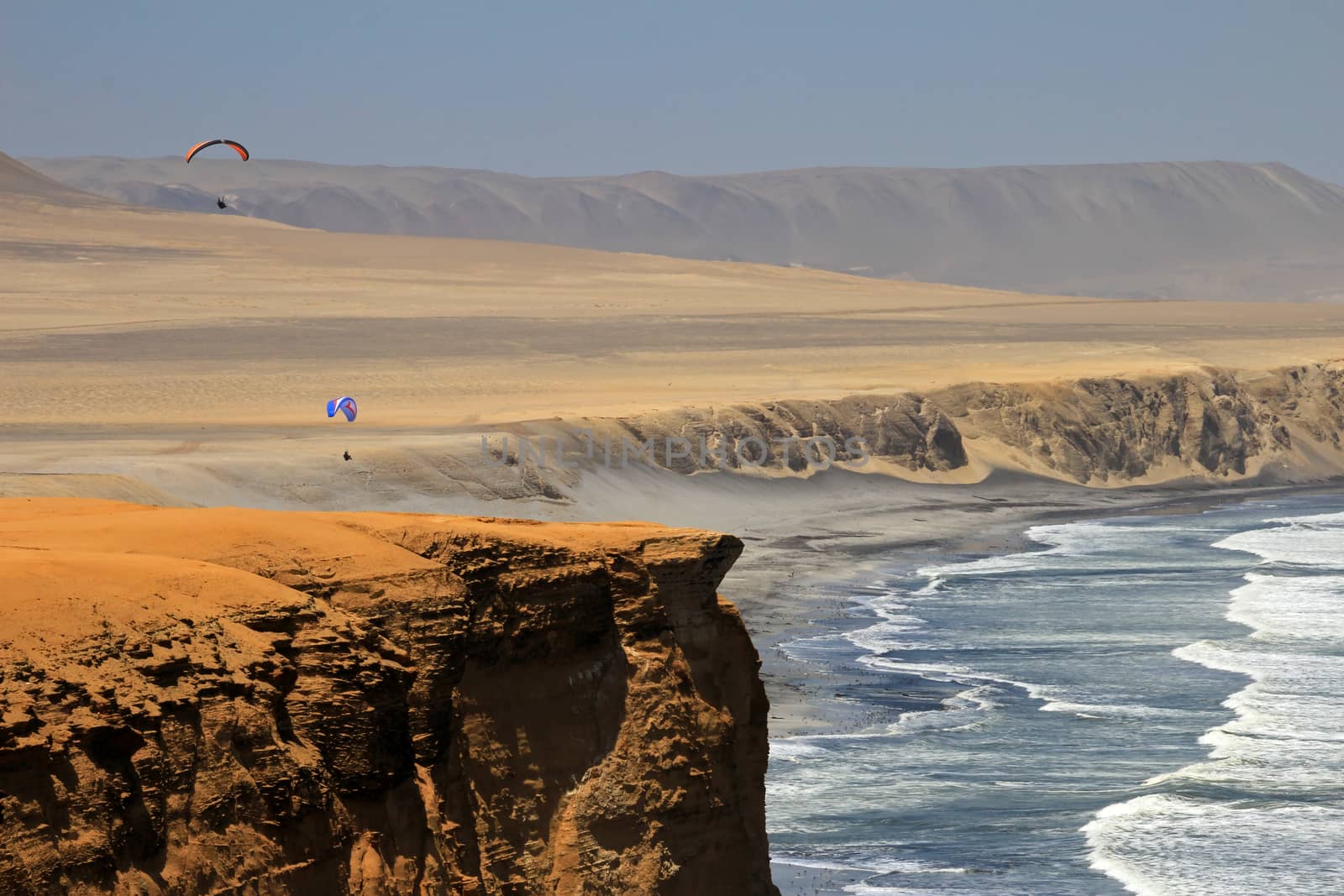 Paraglider soaring over the cliffs at oceanfront of Paracas Peru