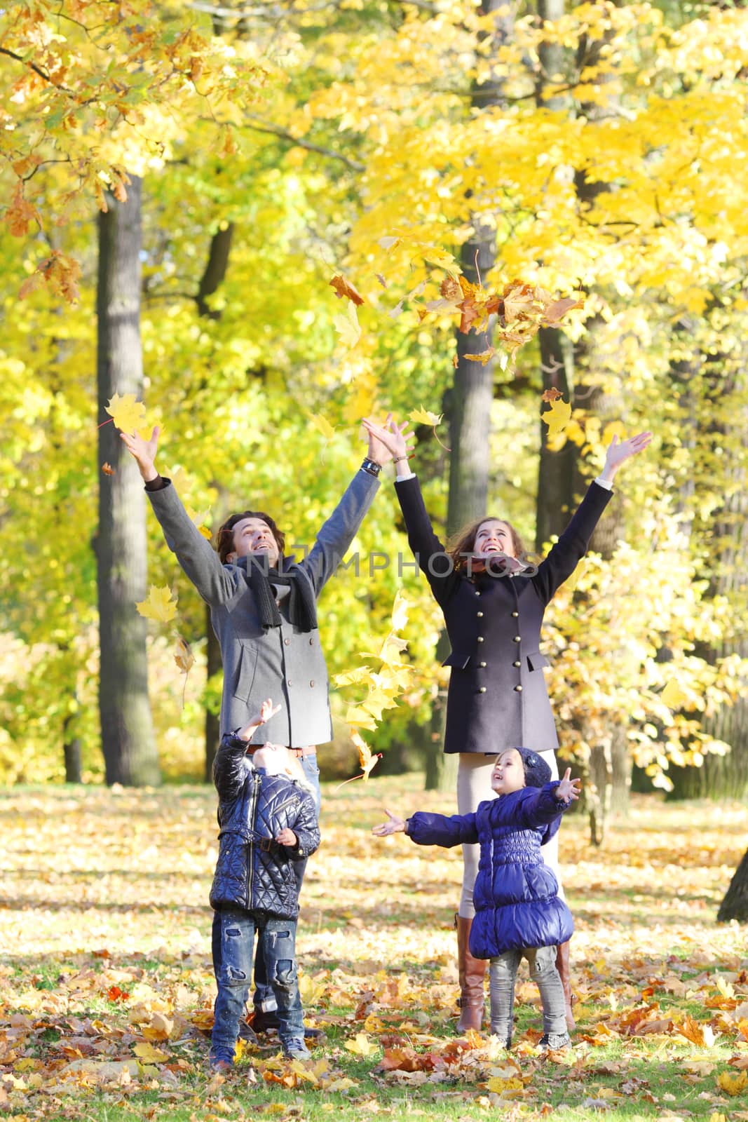 Happy family playing with autumn maple leaves in park