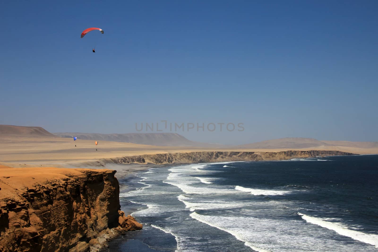 Paraglider soaring over the cliffs at oceanfront of Paracas Peru