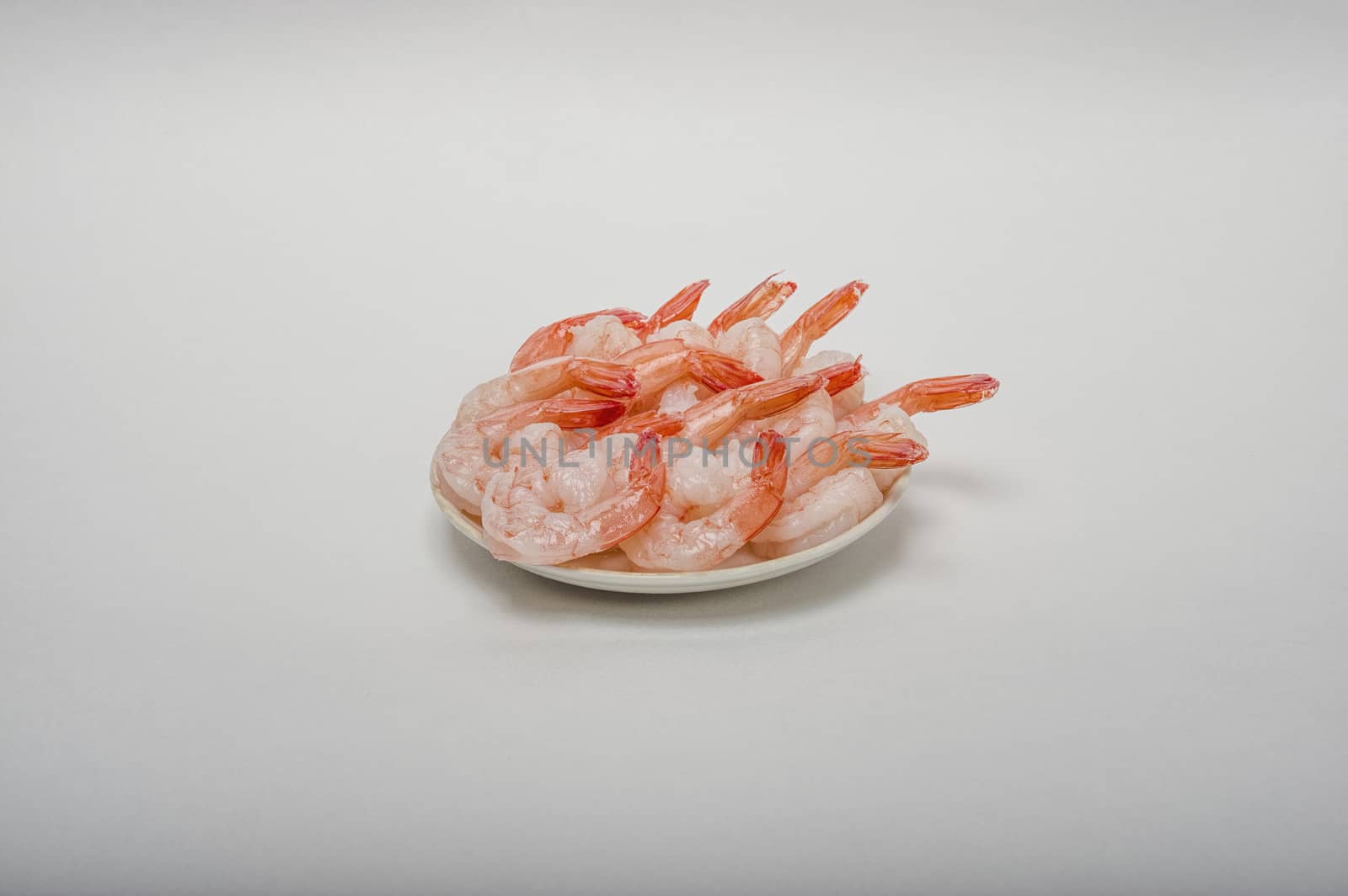 Red peeled prawns lie on a saucer isolated on white background