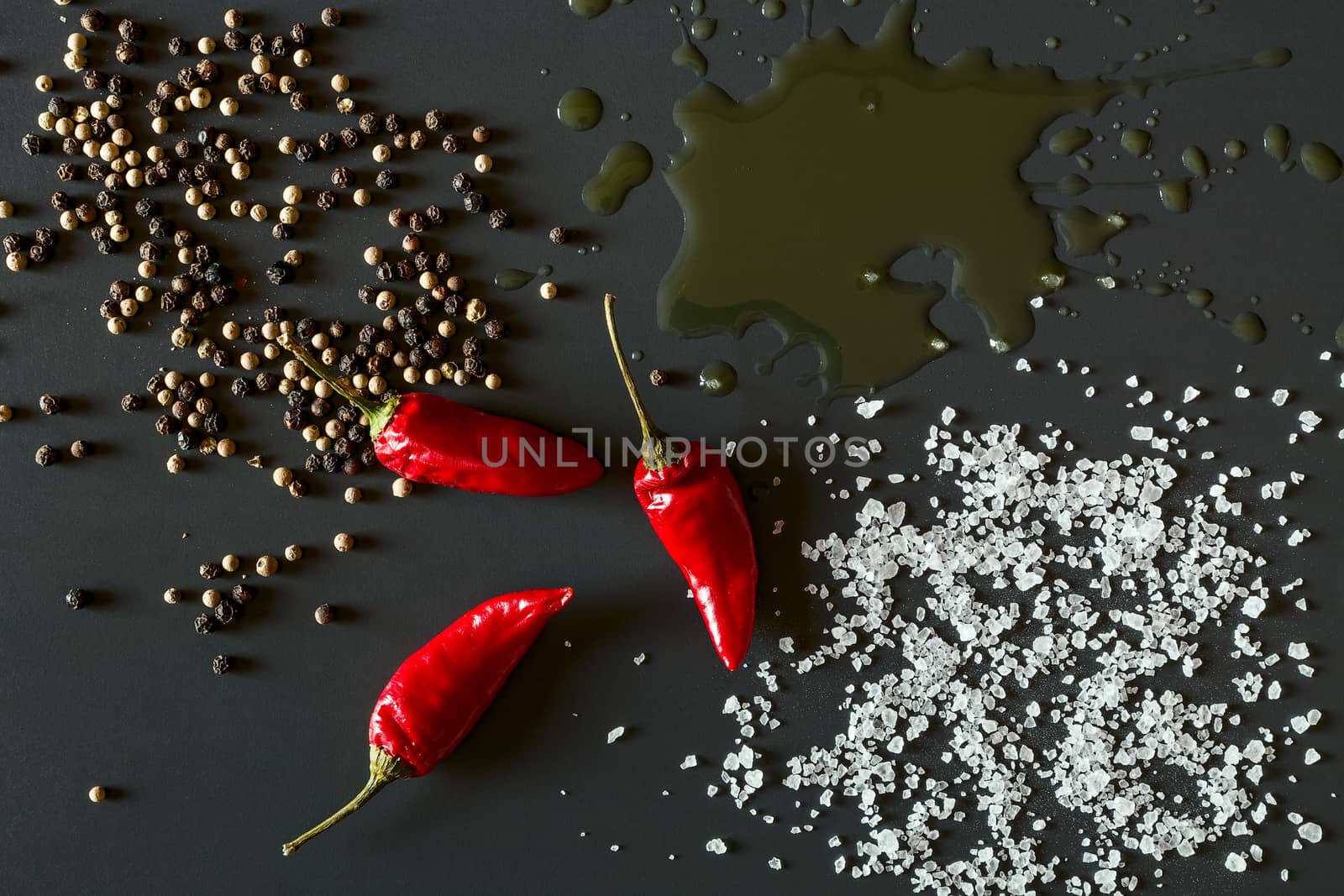 Chili peppers, oil, salt and pepper over a dark background seen from above