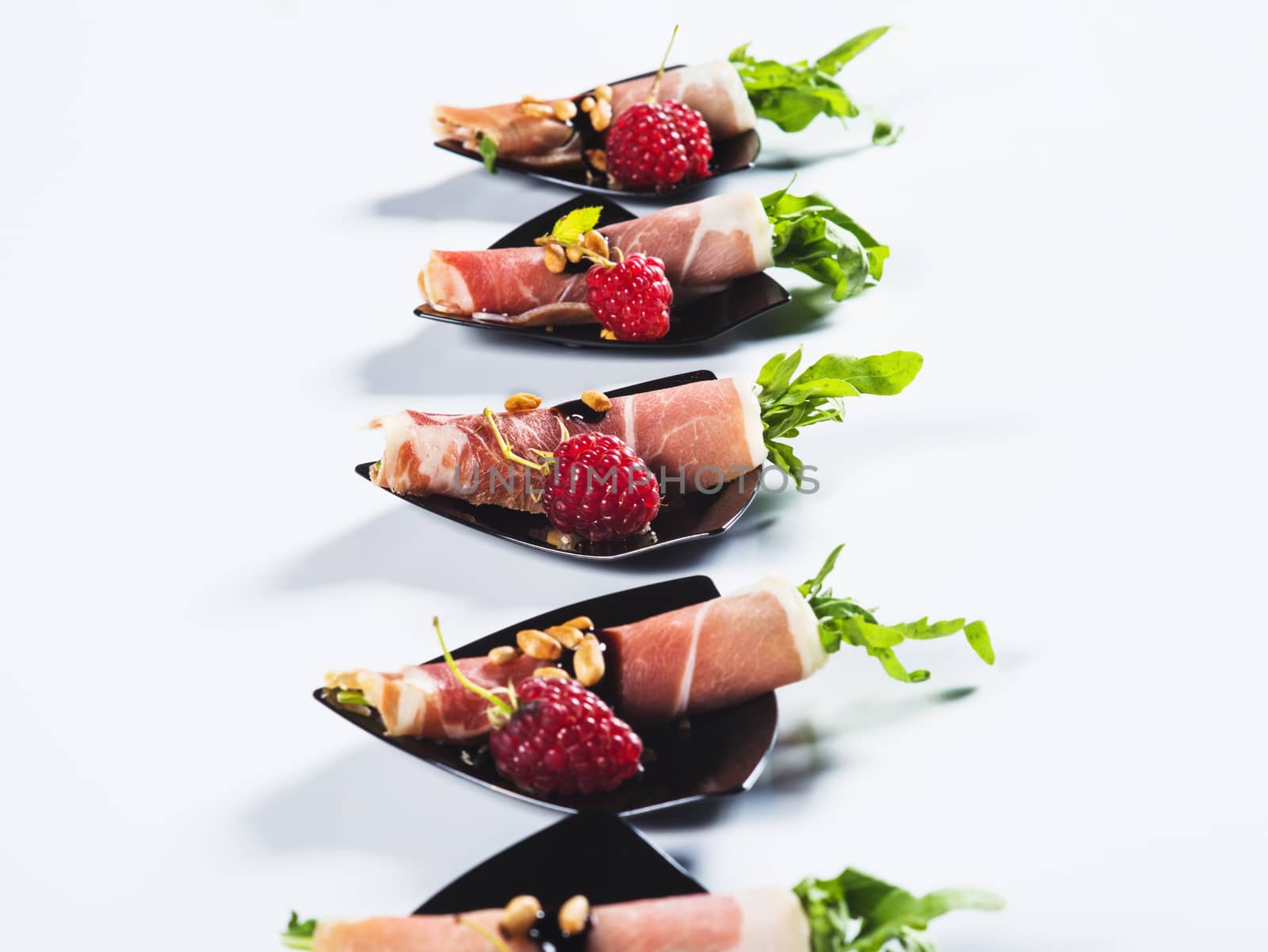 Rolled ham with arugula served with raspberrie on black plate on light background