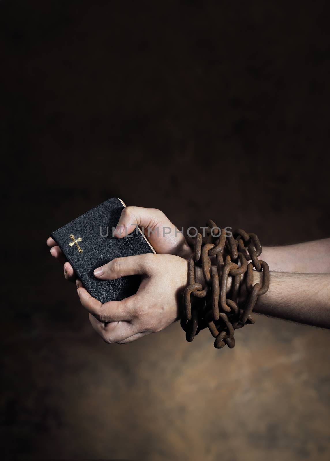 Hands holding a bible tied together with an old rusty chain.