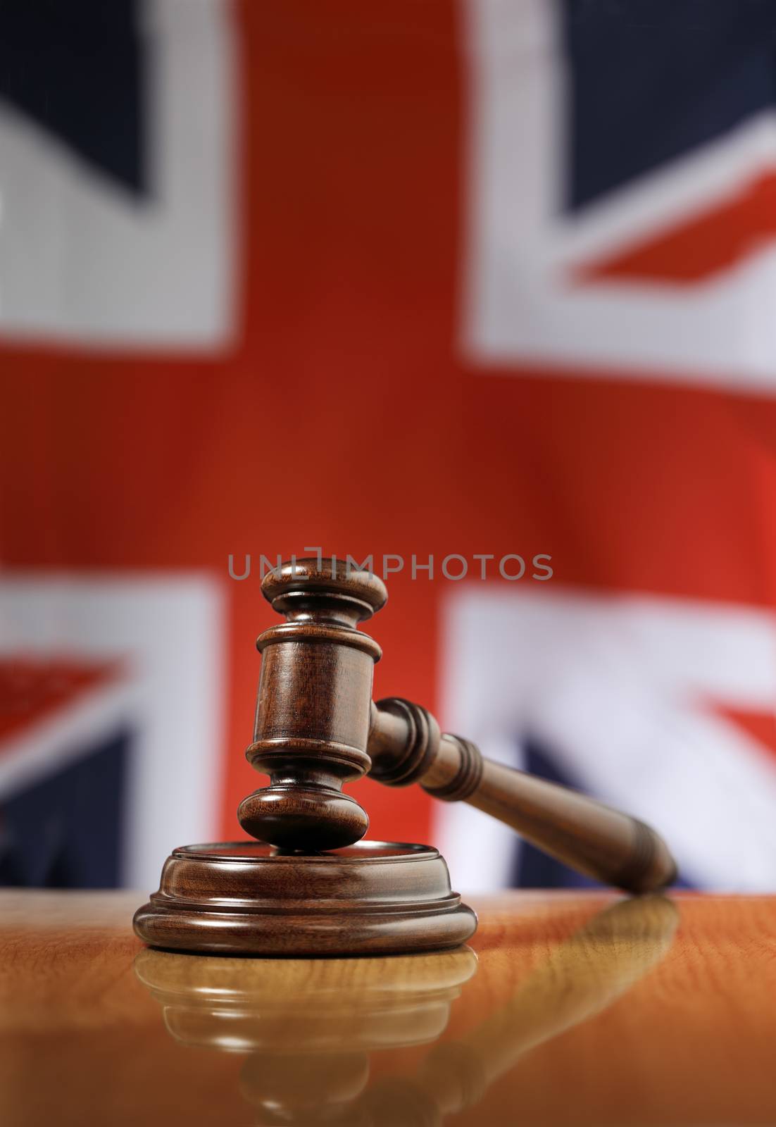 Mahogany wooden gavel on glossy wooden table. Flag of United Kingdom in the background.