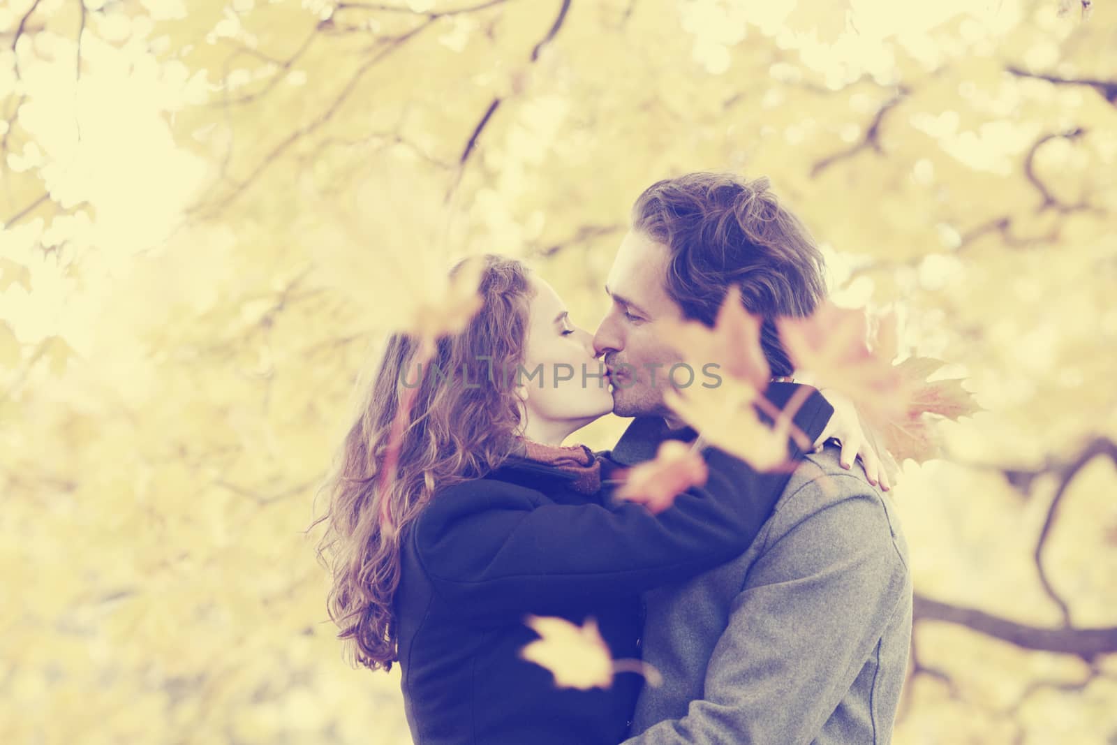 Happy couple kissing in autumn park with yellow trees