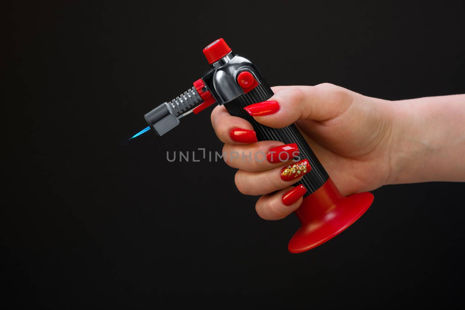 The female hand with beautiful manicure holds a gas torch