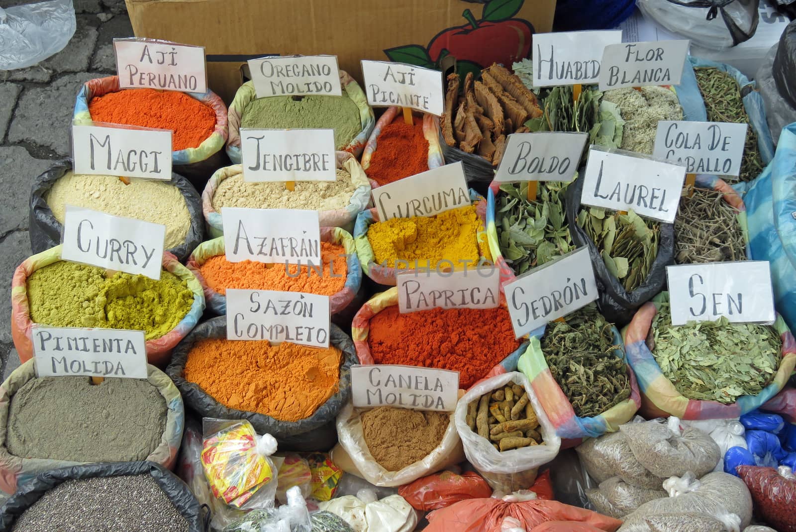 Different bags of colored spices displayed at the andean market of otavalo with signs including each spice