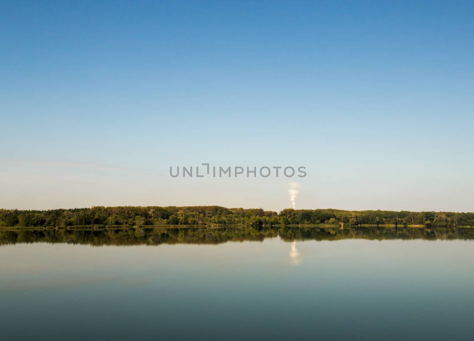 Lanscape image of a lake on a bright cloudless day with forest and a factory on lake's far end