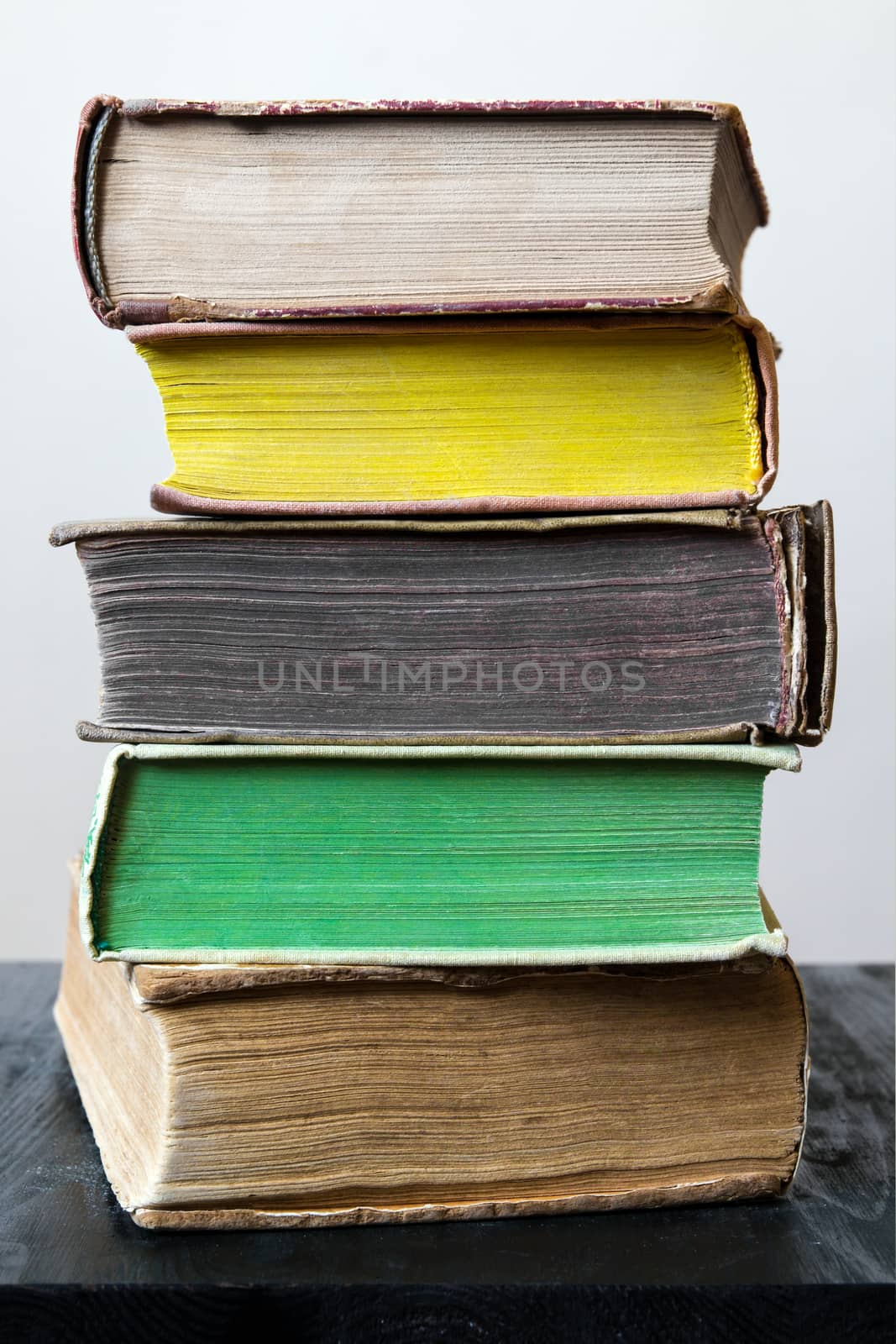 Stack of five old worn books in different colors on black vintage table on light background in natural light