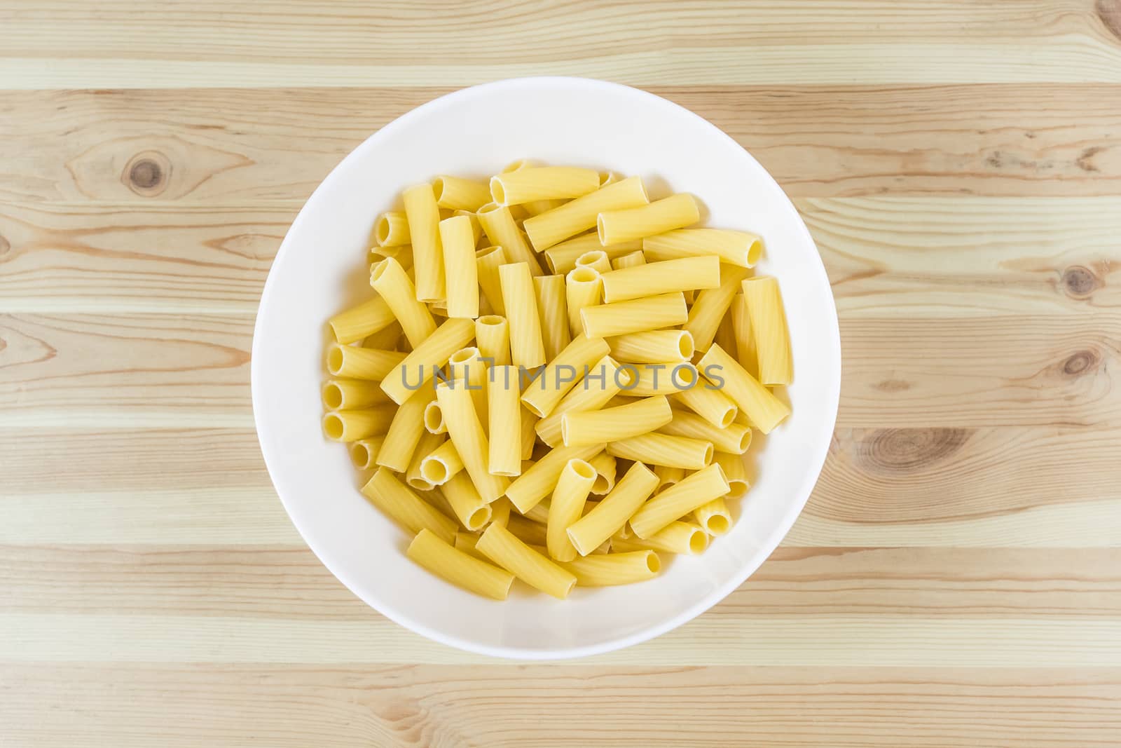 Top view of raw uncooked tortiglioni pasta in white bowl on wood table