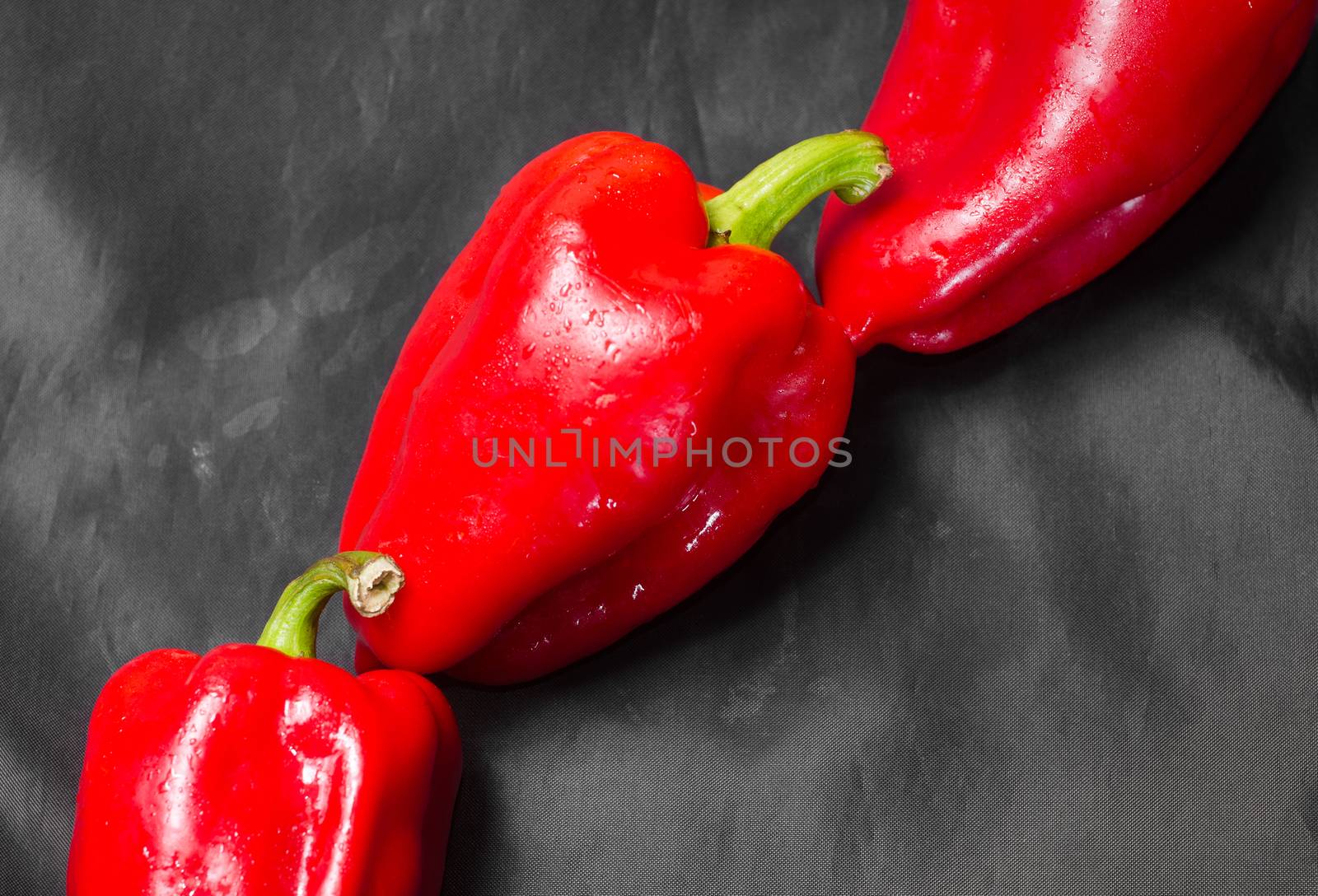 Three red peppers with green tail on a black background. Lie one by one