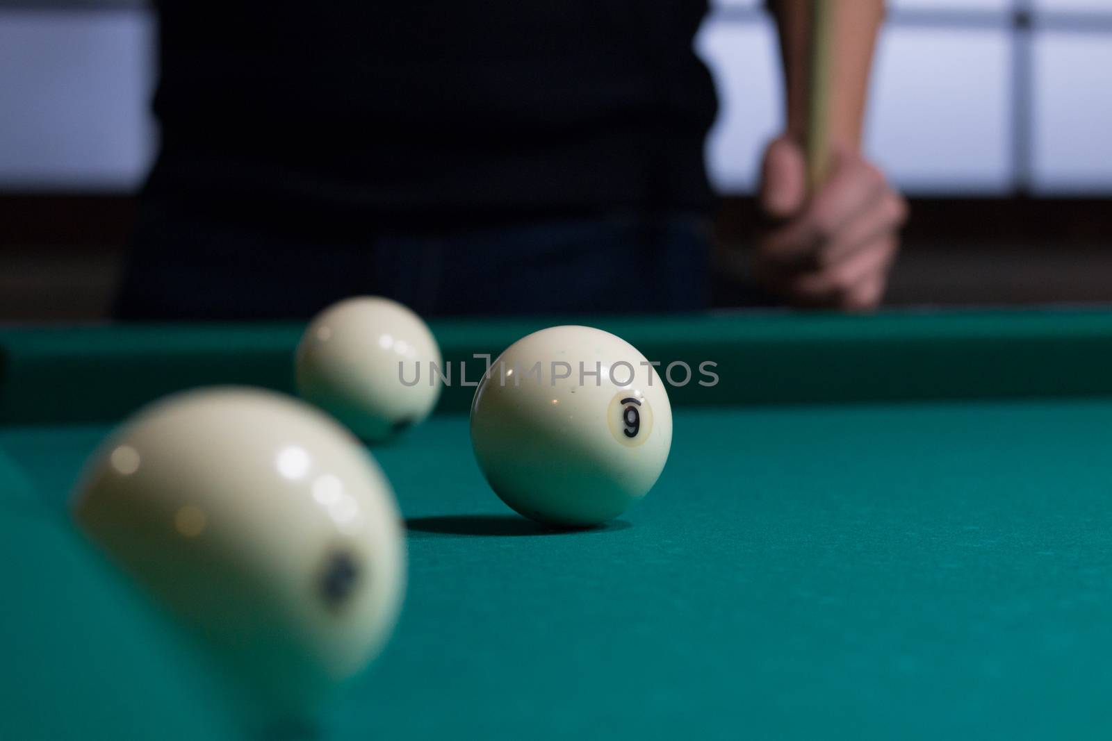 Close-up of Russian billiards game in process: three white balls on green game table cloth and player with cue on background