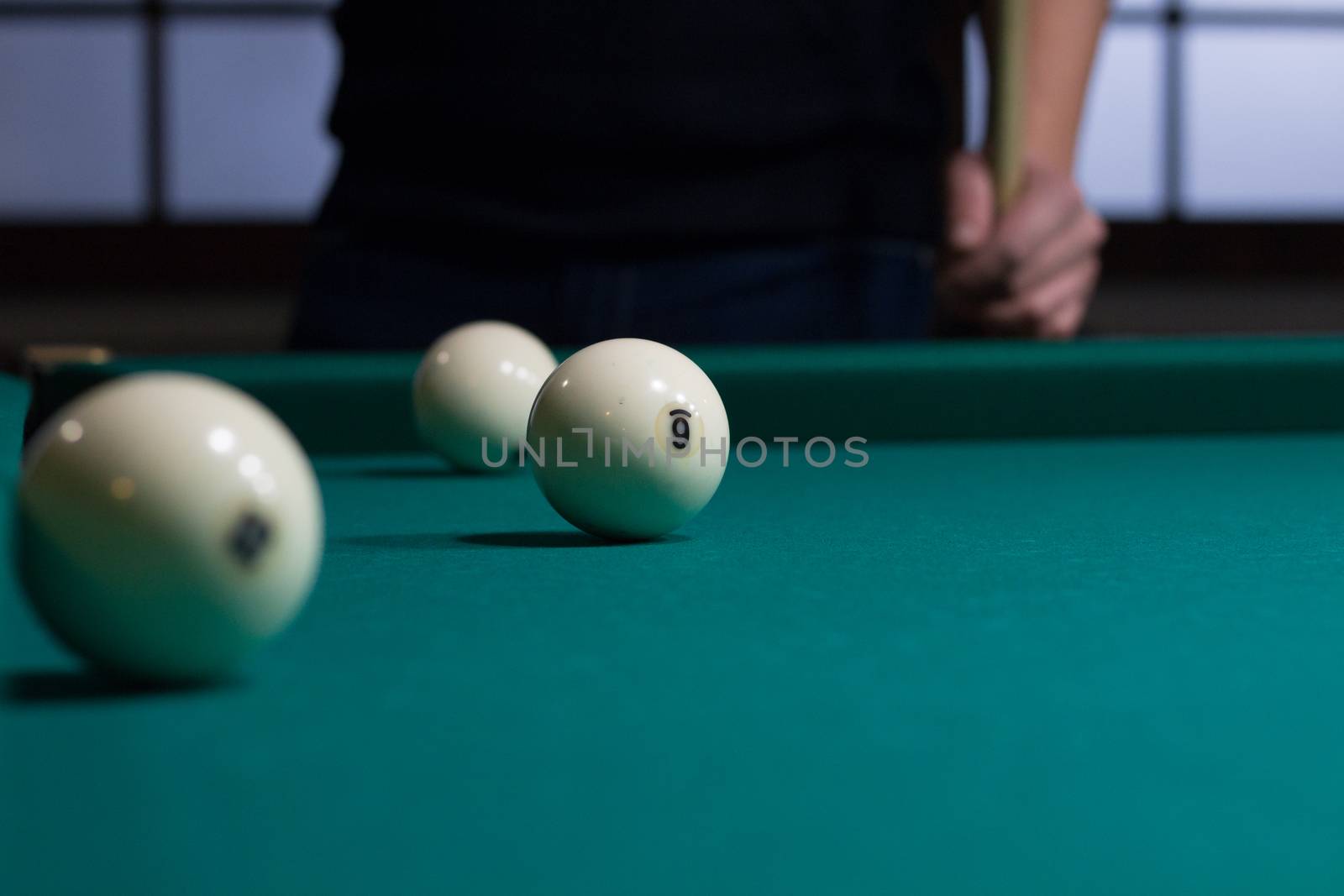 Close-up of Russian billiards game in process: three white balls on green game table cloth and player with cue on background