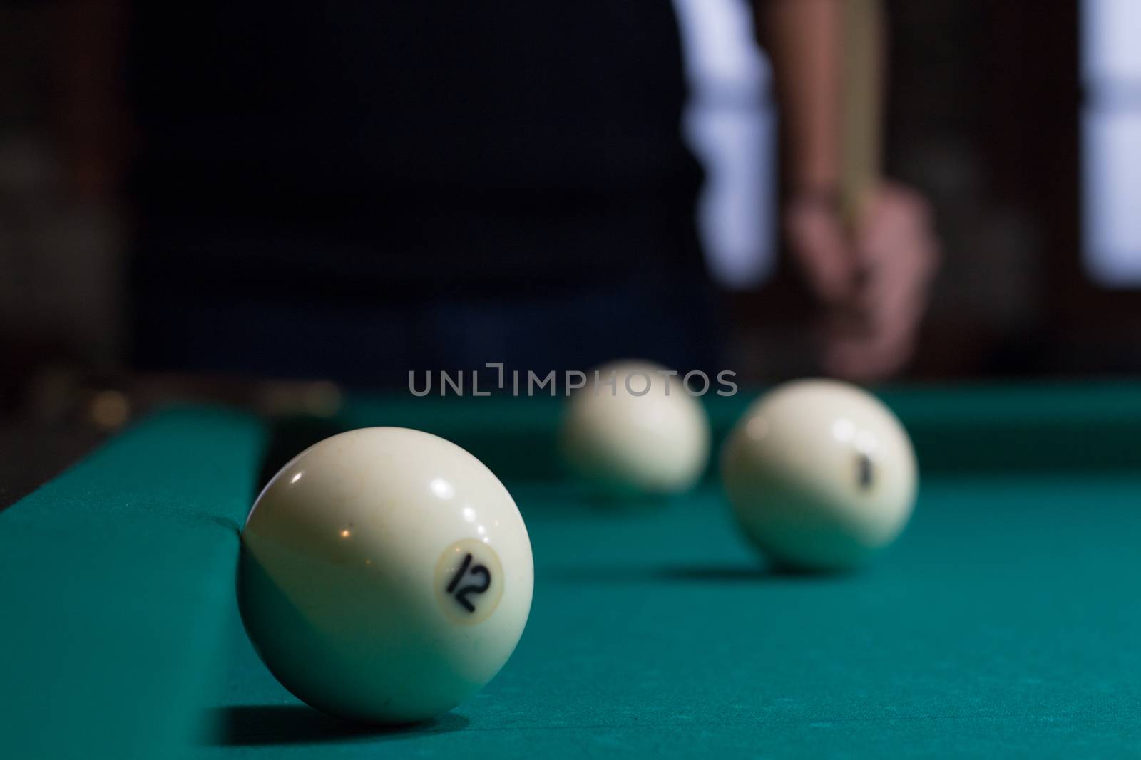 Close-up of Russian billiards game in process: three white balls on green game table cloth and player with cue on background